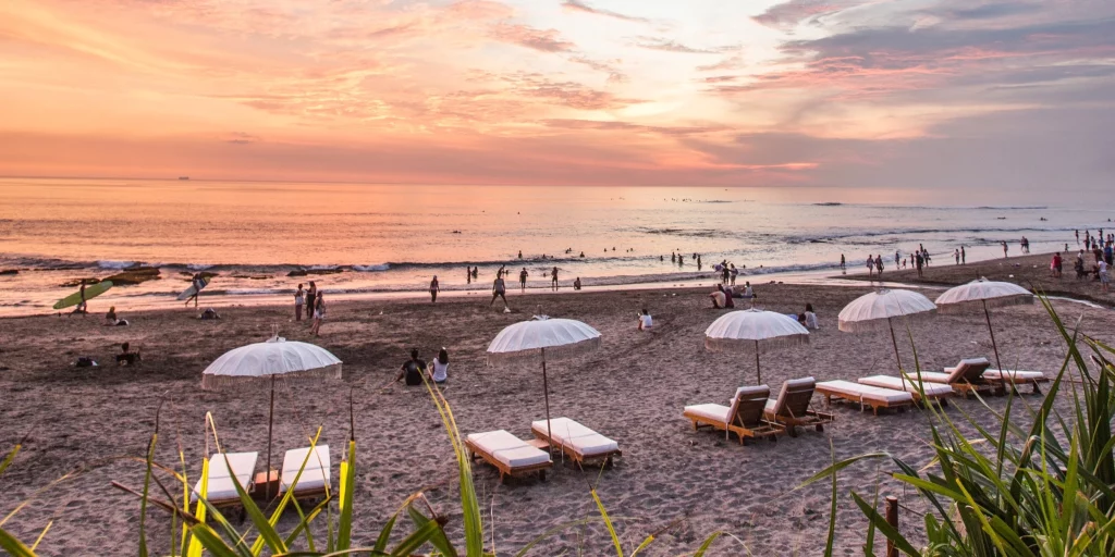 An image of Bali's Canggu beach with people relaxing on the sand and surfing in the ocean.