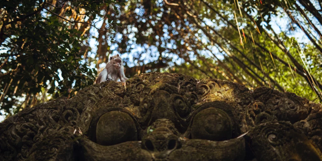 A monkey atop a statue in the Bali Ubud Monkey Forest