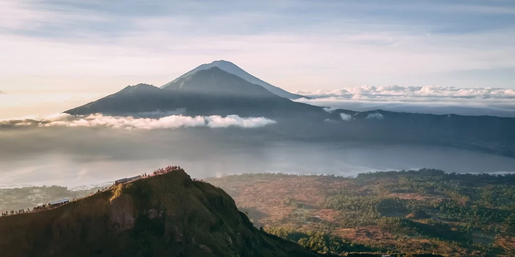 Mount Batur in the background lit by the sunrise. A number of hikers on a peak in the foreground.